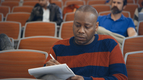 A man in a lecture hall is intently taking notes.