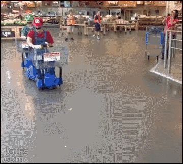 Two dudes dressed up as Mario and Luigi. They're racing around a shopping center (possibly a grocery store) in motorized shopping cart scooters. The one dressed as Mario throws a banana and Luigi runs over it, his cart swerves out of control, and Mario fist pumps in celebration.